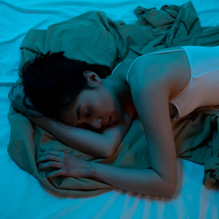 Person lying awake in bed at night in blue light, unable to switch off