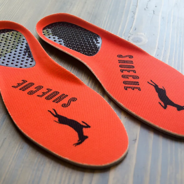 A pair of shoe insoles resting on a wooden floor before being fitted into work shoes