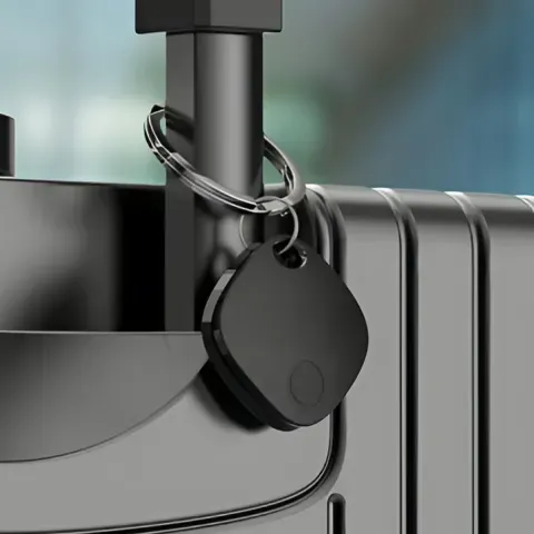 A black iTagPro tracker tag clipped by its key ring to a suitcase handle