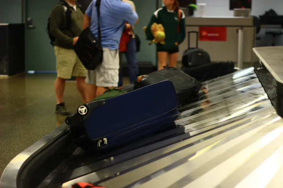 A navy suitcase riding a baggage carousel while travellers wait at baggage claim