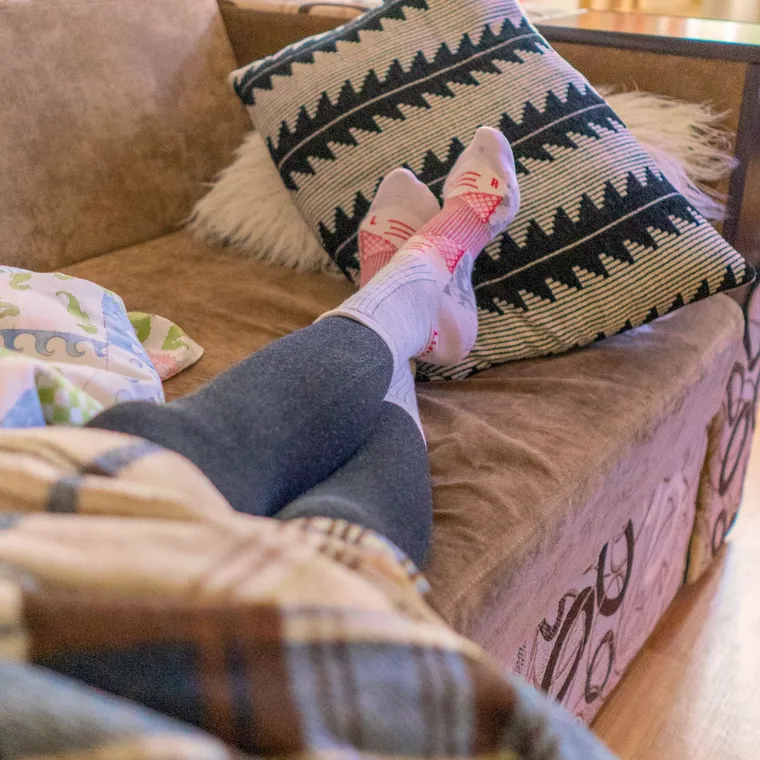 Feet in thick warm socks under a blanket on a sofa in the evening